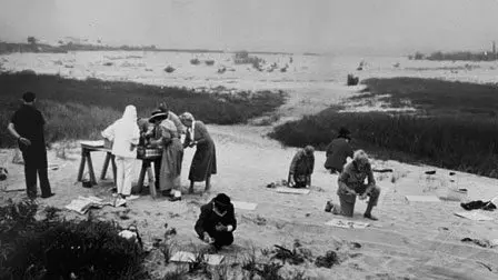 Group of people on a beach, gathered around a table.